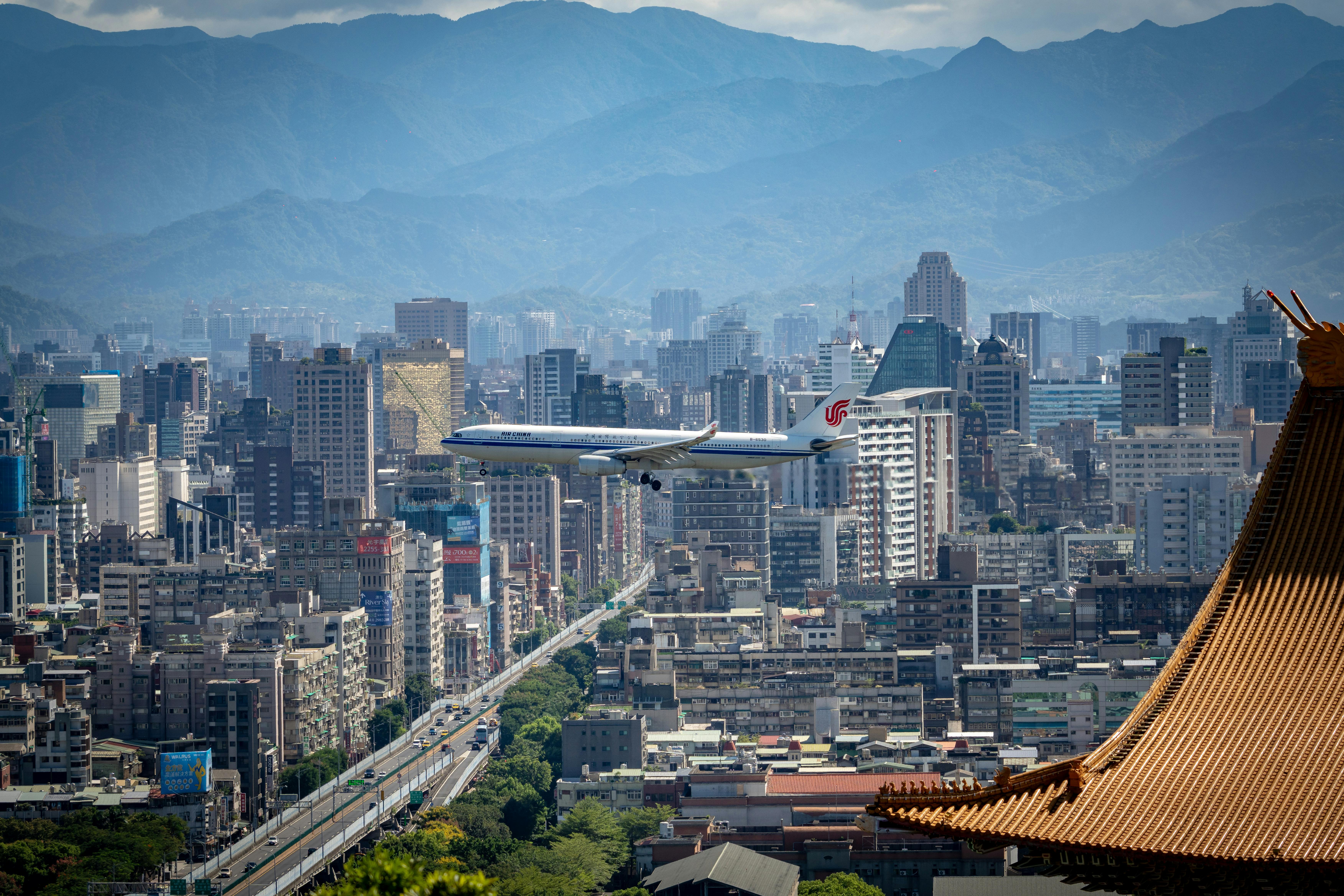 一架商用飞机在山脉为背景的繁华城市景观中飞越，展示城市的繁荣与旅行的魅力
