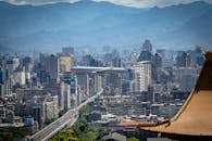 一架商用飞机在山脉为背景的繁华城市景观中飞越，展示城市的繁荣与旅行的魅力