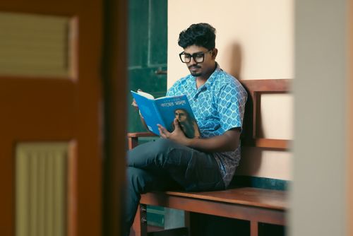 Free A young man sitting on a bench reading a book indoors. Calm and focused study environment. Stock Photo