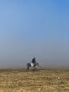 在晴朗的蓝天下，一名孤独的骑马者穿越迷雾开阔的草原