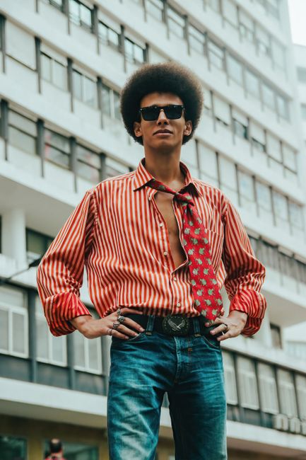 Fotomural Joven con atuendo retro y gafas de sol, posando en un entorno urbano al aire libre.