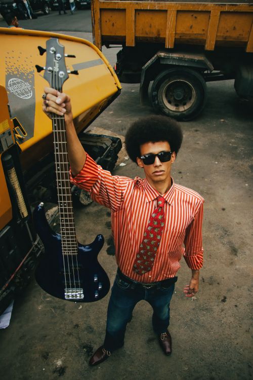 Free Young man with afro holding a bass guitar, showcasing style and music potential in an urban outdoor setting. Stock Photo