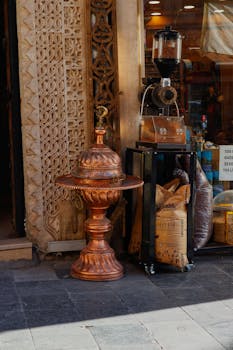 Charming coffee shop entrance with ornate copper vessel and rustic grinder outside.