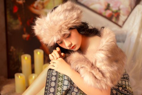 Free Young woman in a fur hat and shawl with candles indoors, embracing warmth and coziness. Stock Photo