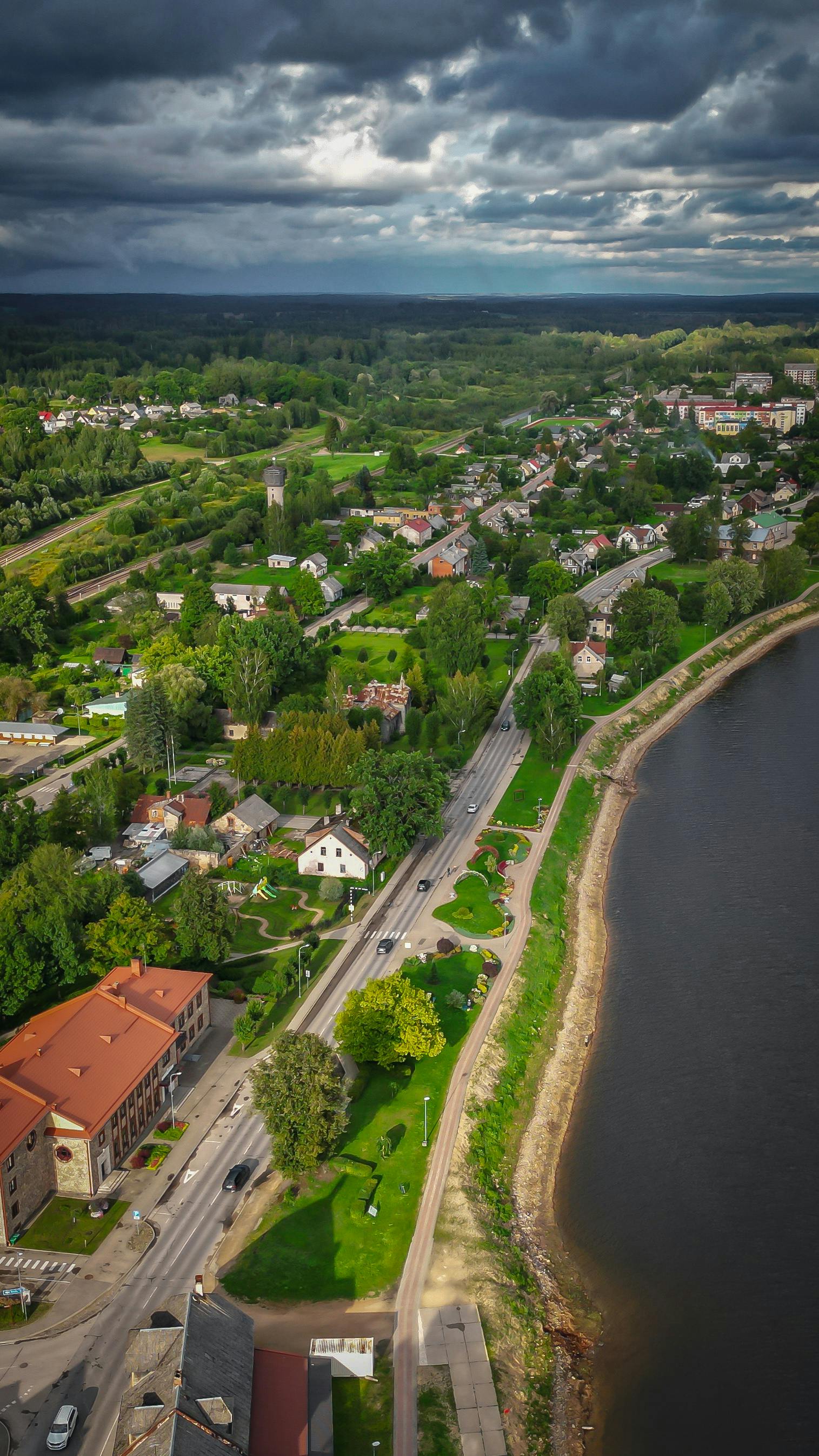 Scenic aerial view capturing a town nestled by a river under dramatic skies, showcasing lush greenery.
