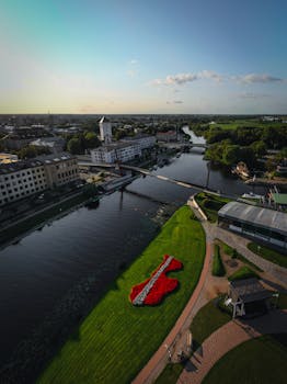 航拍视角下，河边城市的景象一览无余，前景中的花卉点缀其间，彰显出城市的美