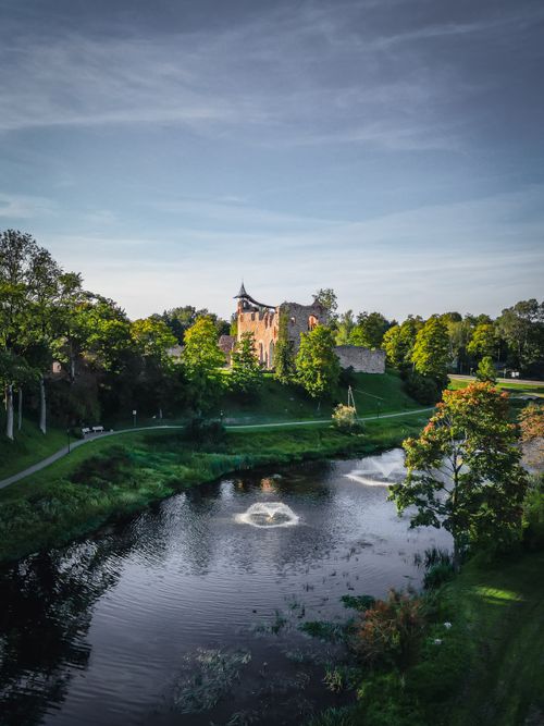 Free A picturesque medieval castle surrounded by lush greenery and a reflective river under a blue sky. Stock Photo