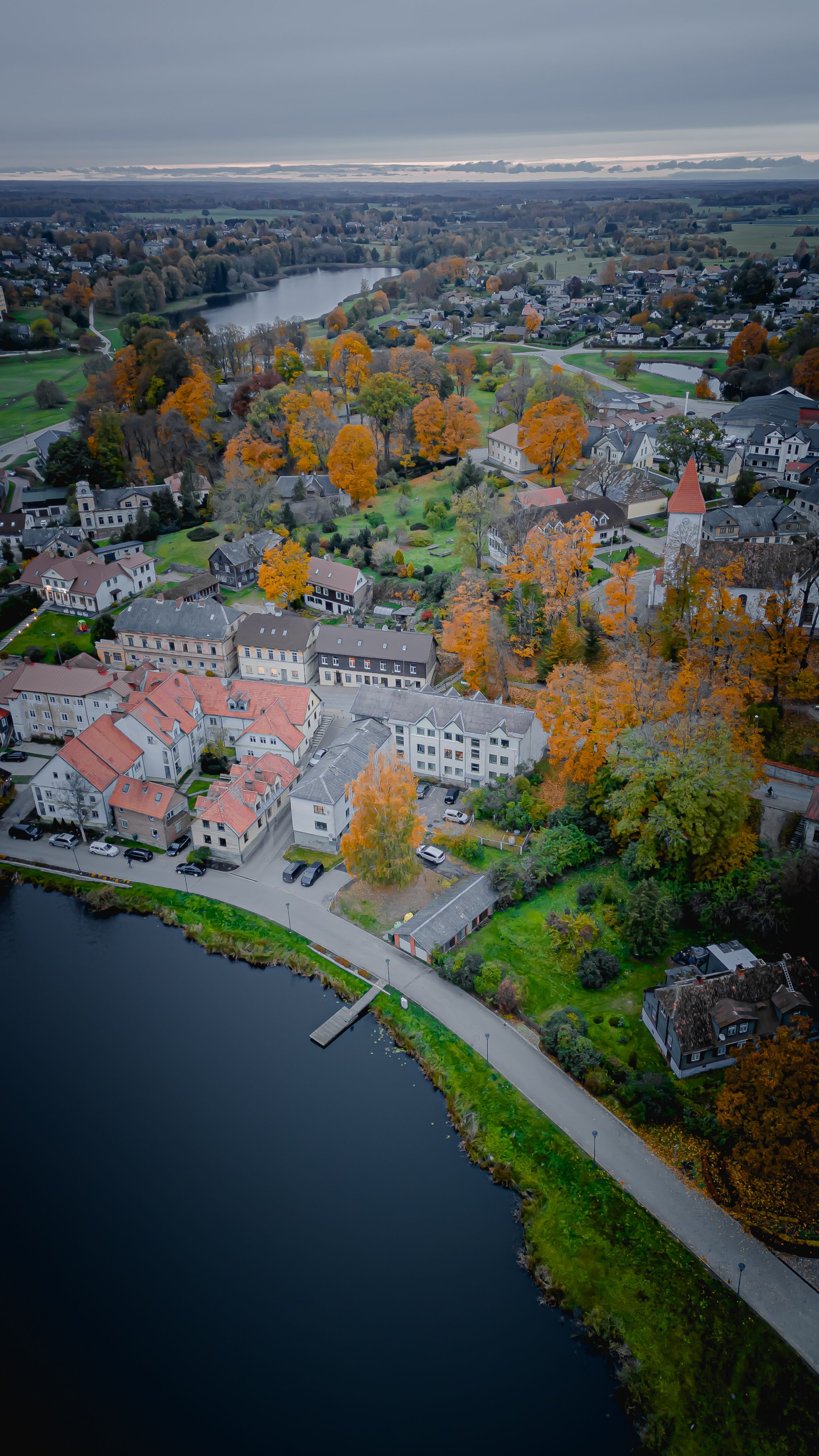 A picturesque village with autumn foliage by a lake, captured from above.