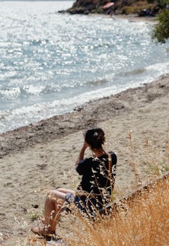 一个女人在海滩上享受宁静的一天，坐在波光粼粼的大海旁