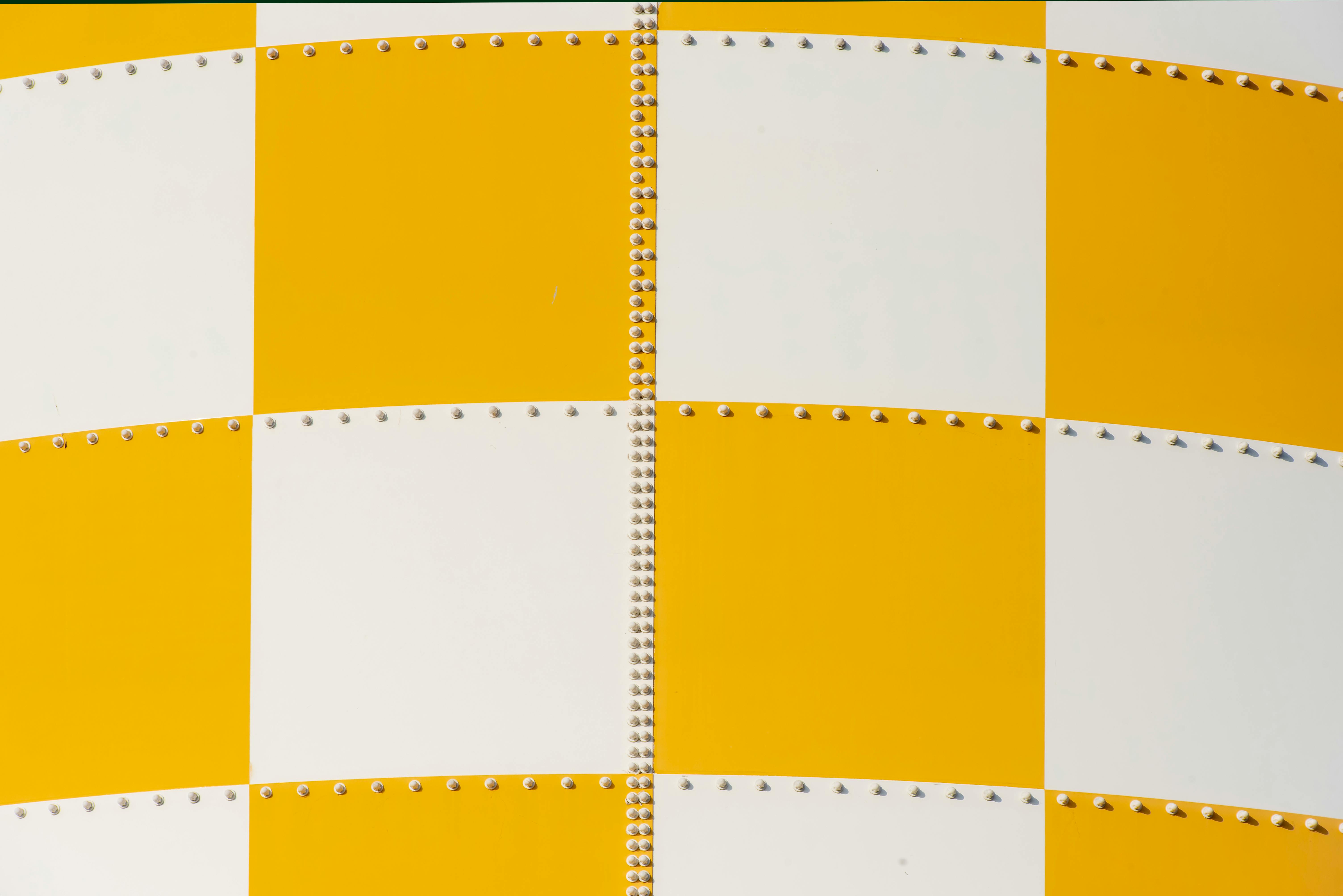Close-up of a yellow and white checkered metal panel, featuring rows of rivets.