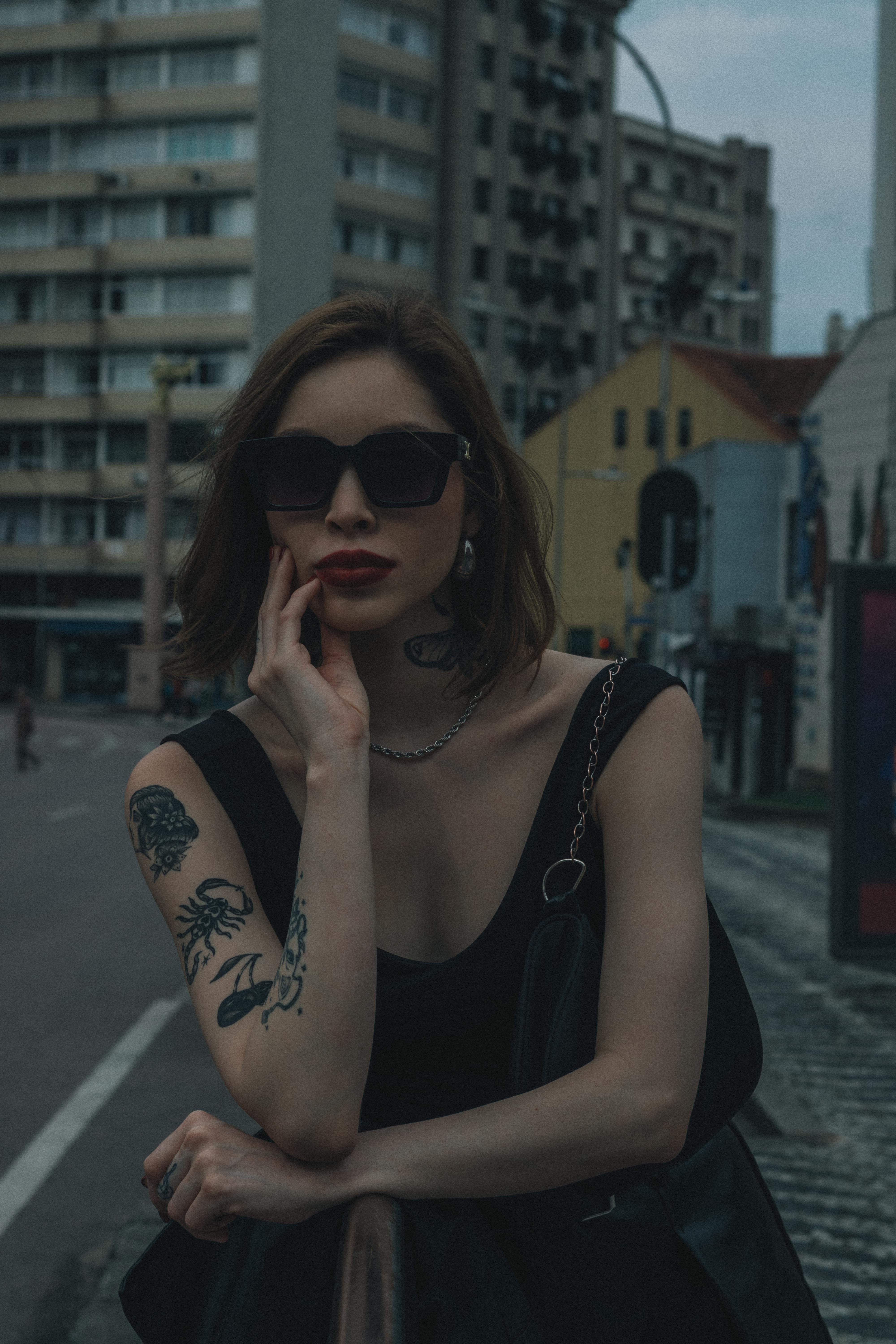 Безкоштовне Модна жінка з сонцезахисними окулярами та татуюваннями в міському пейзажі. стокове фото
