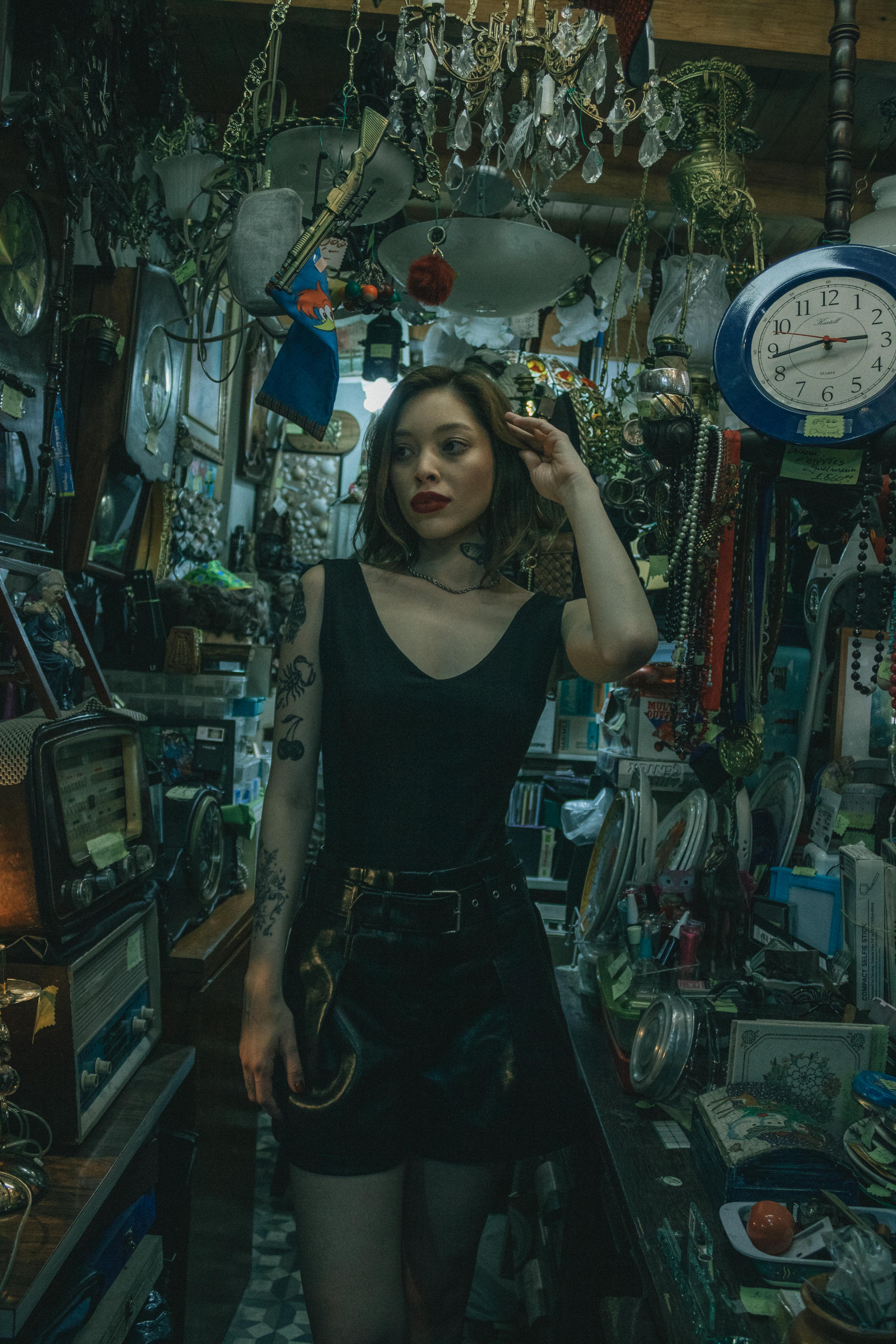 ingyenes Stílusos nő áll egy eklektikus vintage boltban, antik tárgyakkal körülvéve. Stockfotó