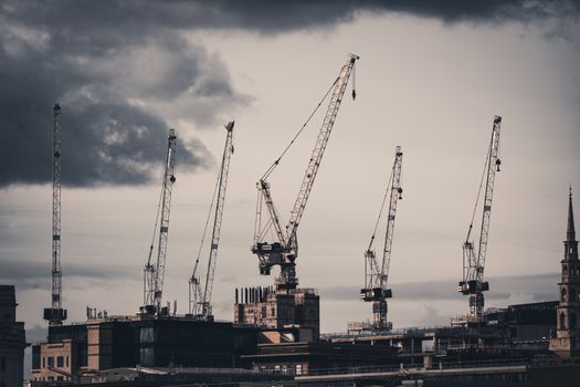 Dramatic London skyline featuring construction cranes and stormy clouds during an urban transformation.