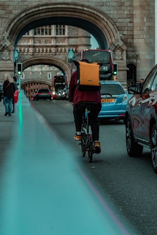 Free A cyclist rides across Tower Bridge in London amidst evening traffic, showcasing urban life. Stock Photo