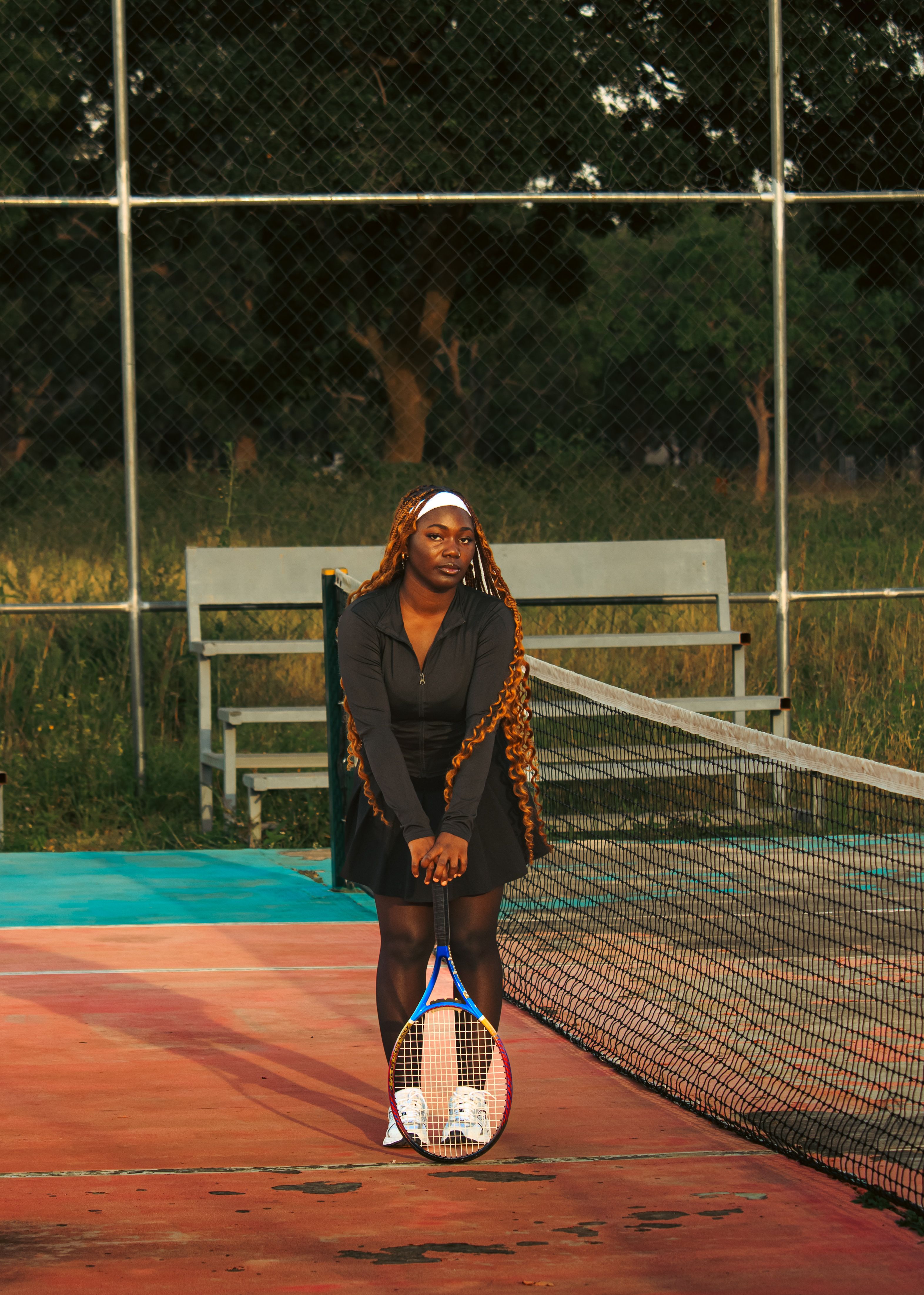 Confident young woman standing on a tennis court with a racket, showcasing athletic style and determination.