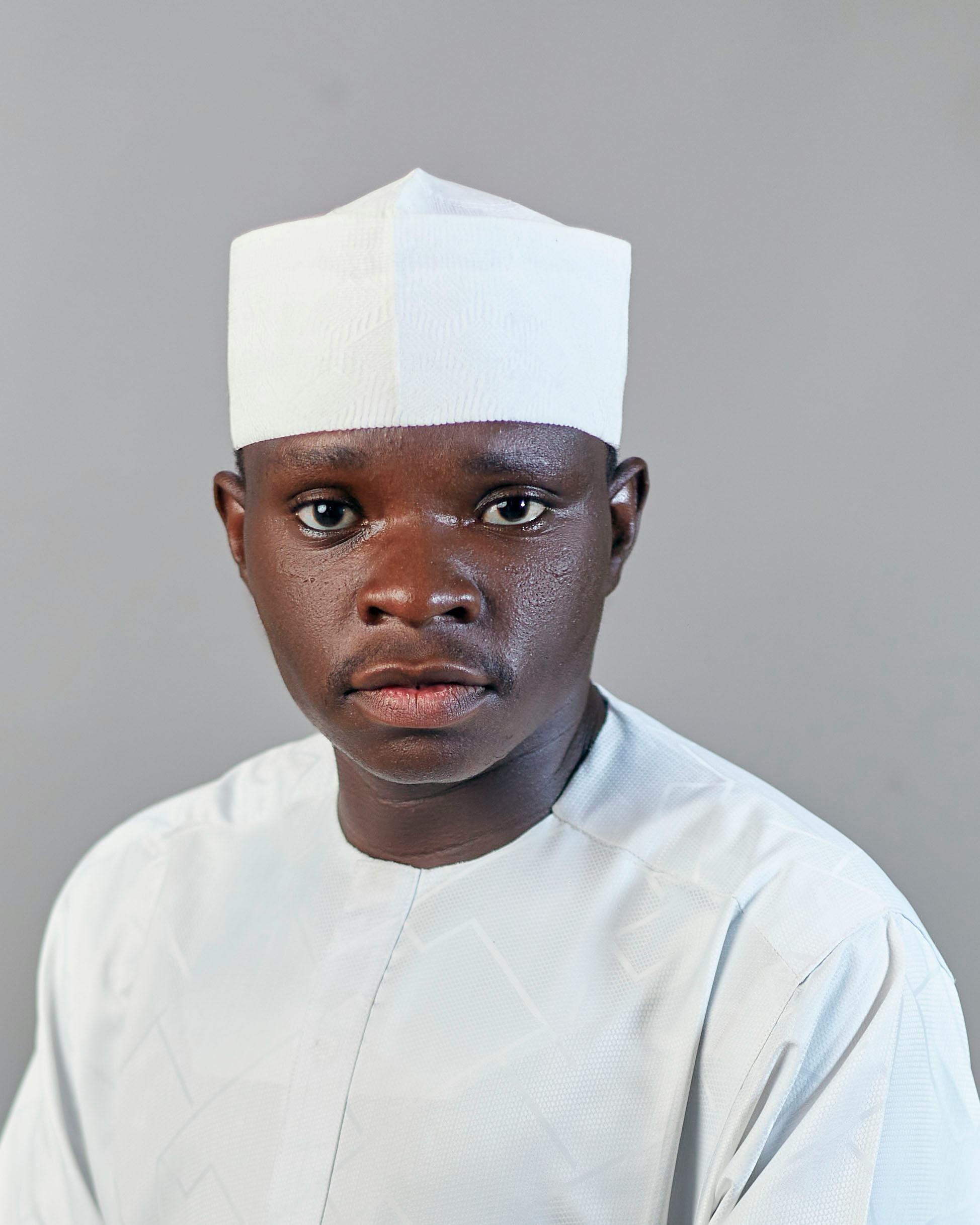 Studio portrait of an adult man wearing traditional white attire against a gray background.