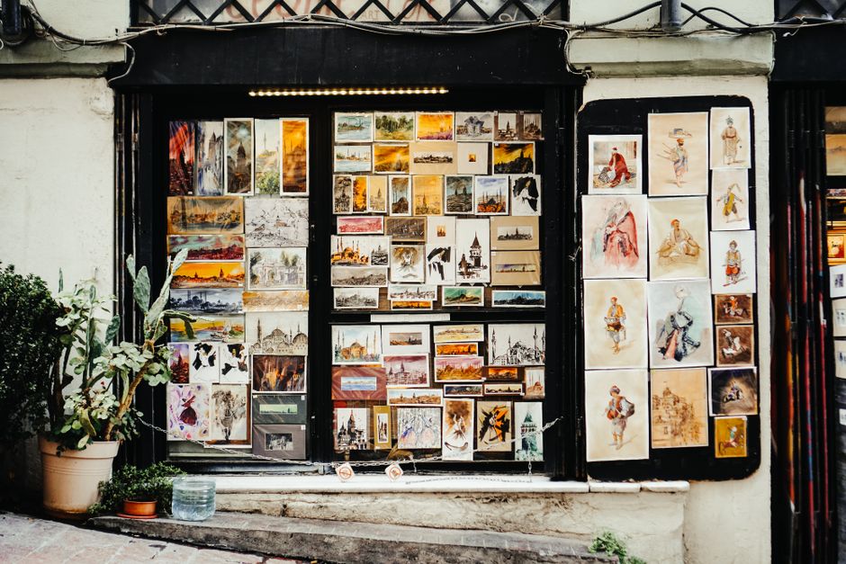 Vibrant art gallery window showcasing diverse paintings and sketches in an urban outdoor street setting.