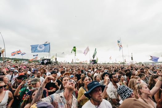 A lively crowd enjoying the Glastonbury Festival in England, with flags waving across the sky.