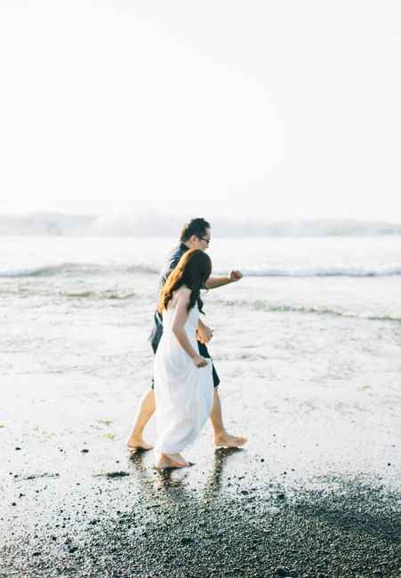 A couple enjoys a romantic walk along a sandy beach by the sea under bright daylight.