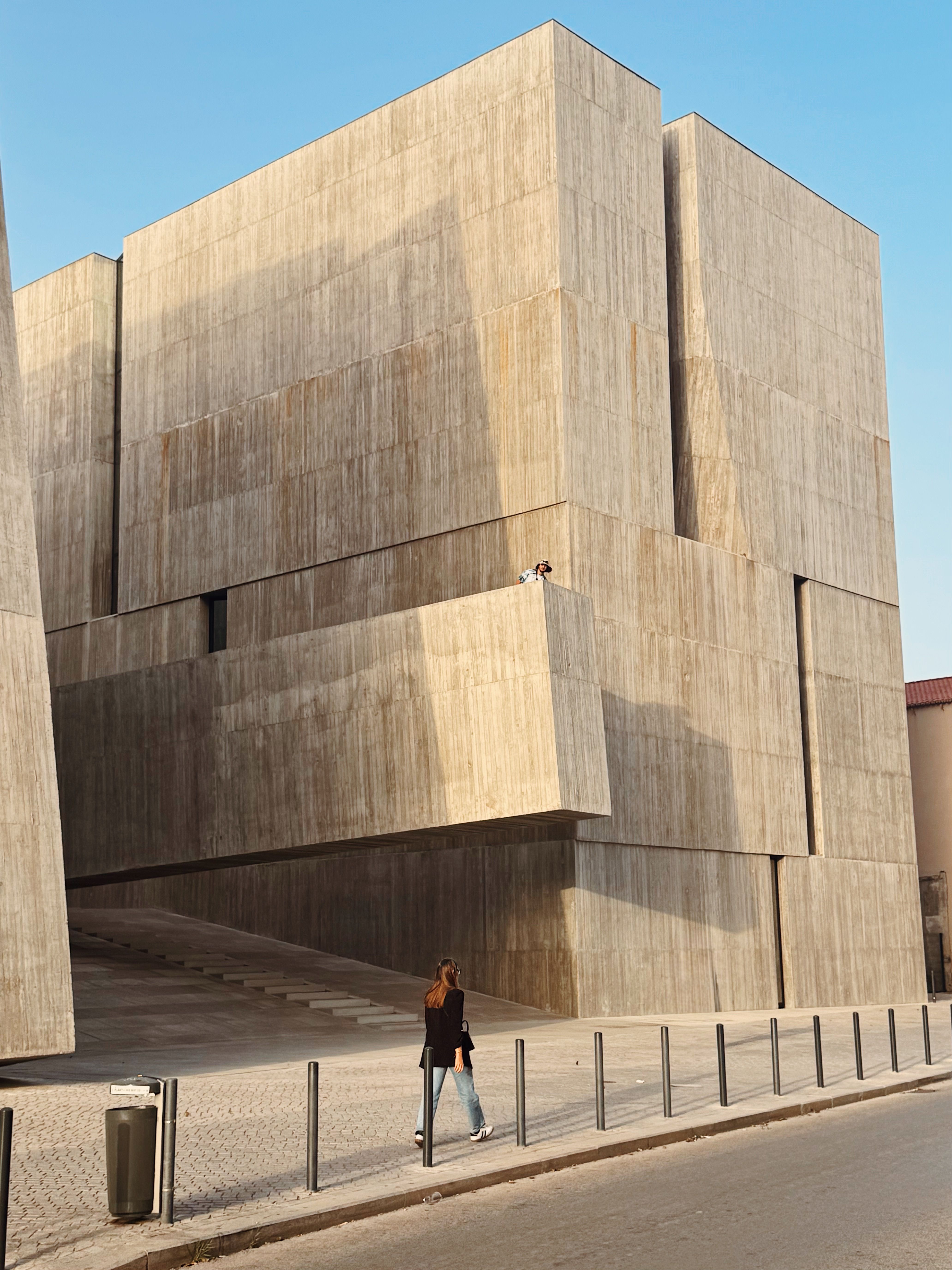 A modern concrete building with a person walking by, showcasing contemporary architecture.. modern, concrete, building