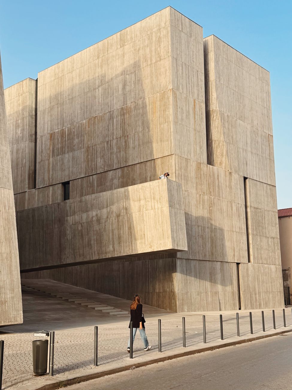 A modern concrete building with a person walking by, showcasing contemporary architecture.. modern, concrete, building