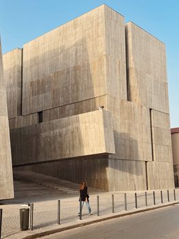 A modern concrete building with a person walking by, showcasing contemporary architecture.. modern, concrete, building