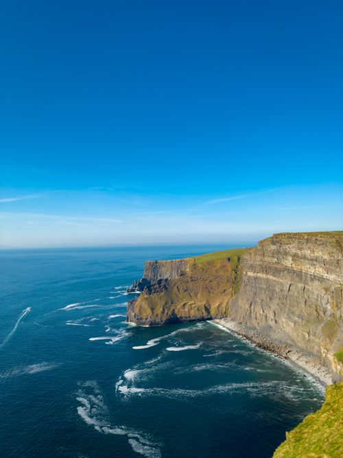 Free Scenic view of the iconic Cliffs of Moher in Ireland, with clear blue skies and vibrant ocean waves. Stock Photo