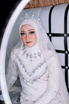 Beautiful bride in a detailed white wedding dress and hijab adorned with jewels, creating a regal look.