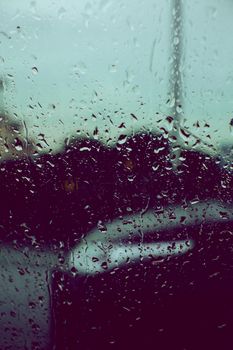 Closeup of raindrops on glass with blurred city background, creating a moody urban scene.