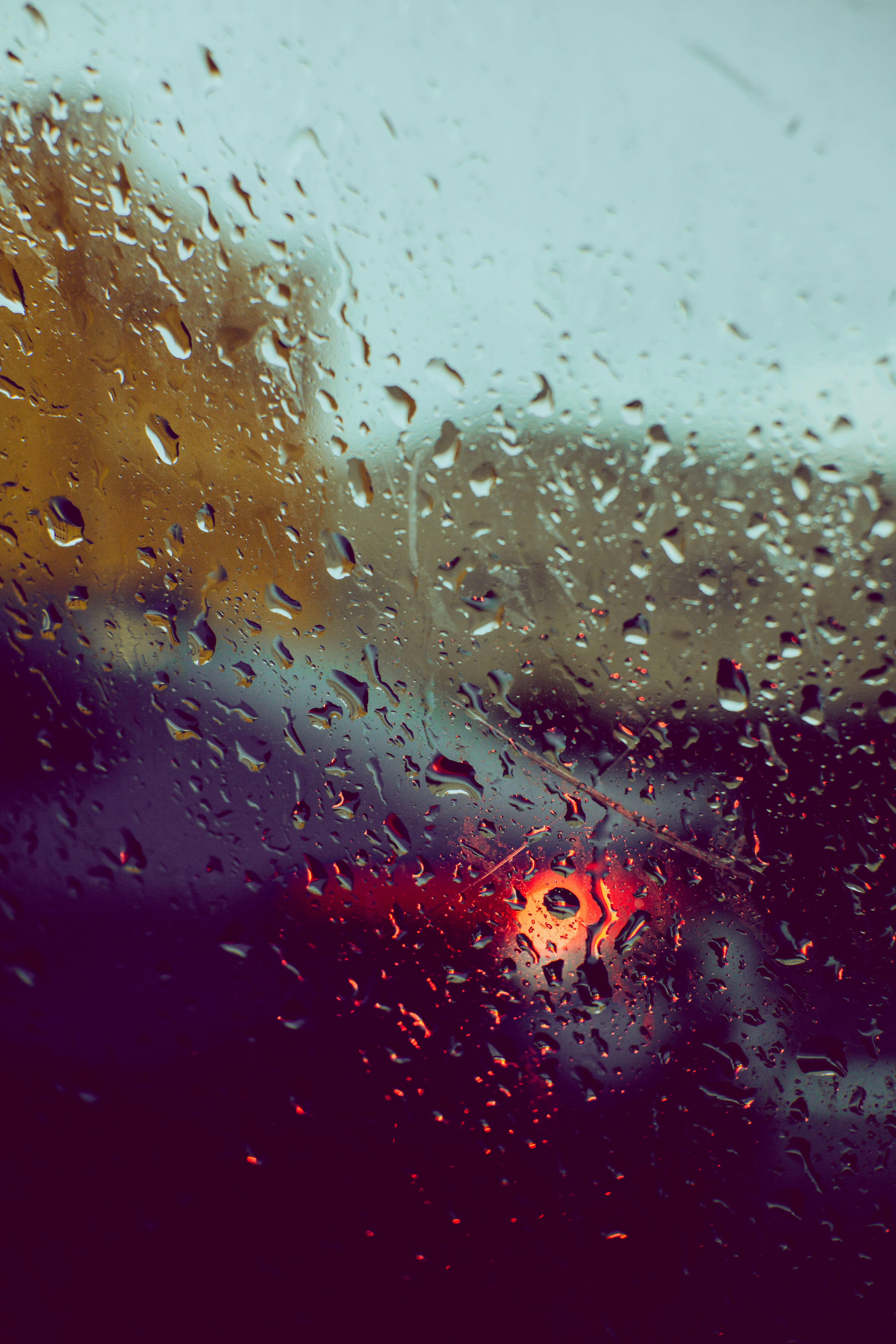 Blurred car tail lights seen through a rain-covered window, creating a moody evening scene.