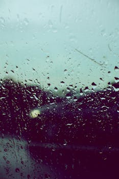 Raindrops on a window with blurred lights from passing cars, conveying a moody atmosphere.