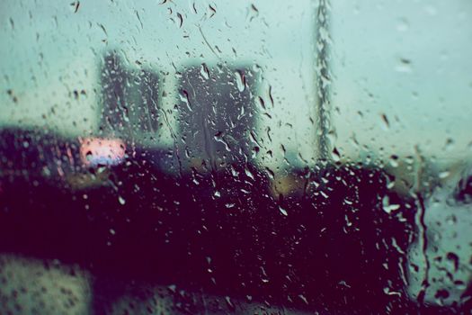 Raindrops on a window, with a blurred cityscape in the background, evoke a moody atmosphere.