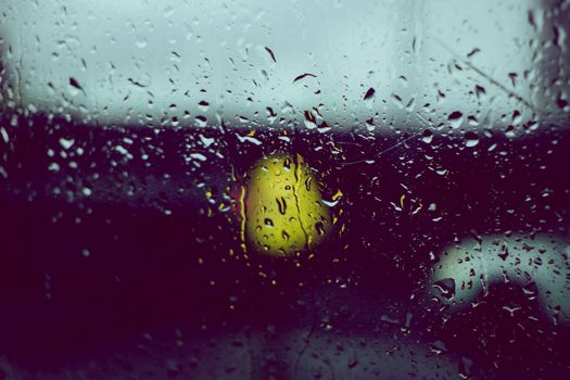 Close-up of raindrops on a window with blurred city lights in the background.