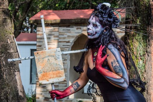 A Catrina makeup model poses in a Mexican cemetery, celebrating Día de Muertos.