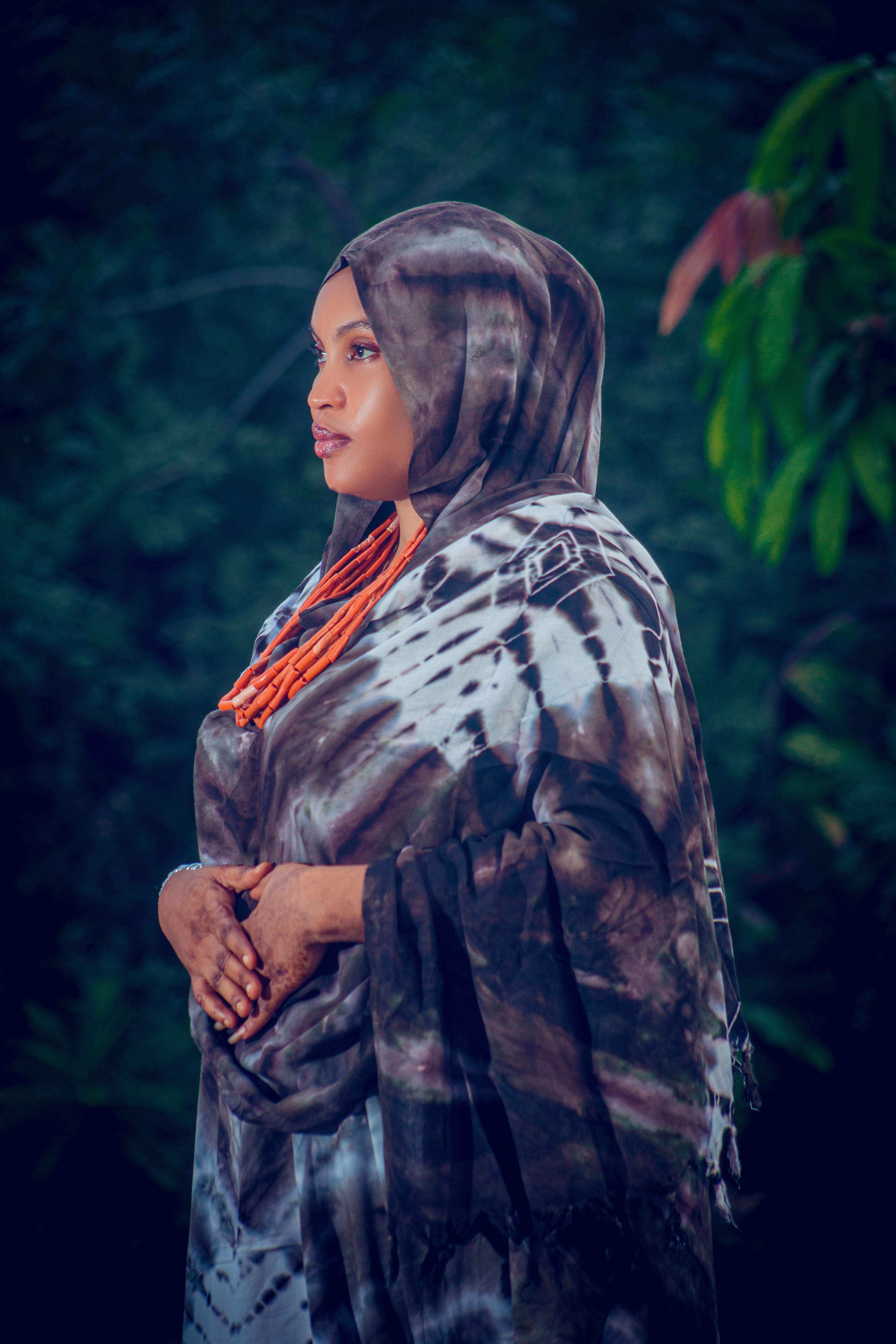 Woman in colorful traditional attire and hijab posing outdoors with thoughtful look.