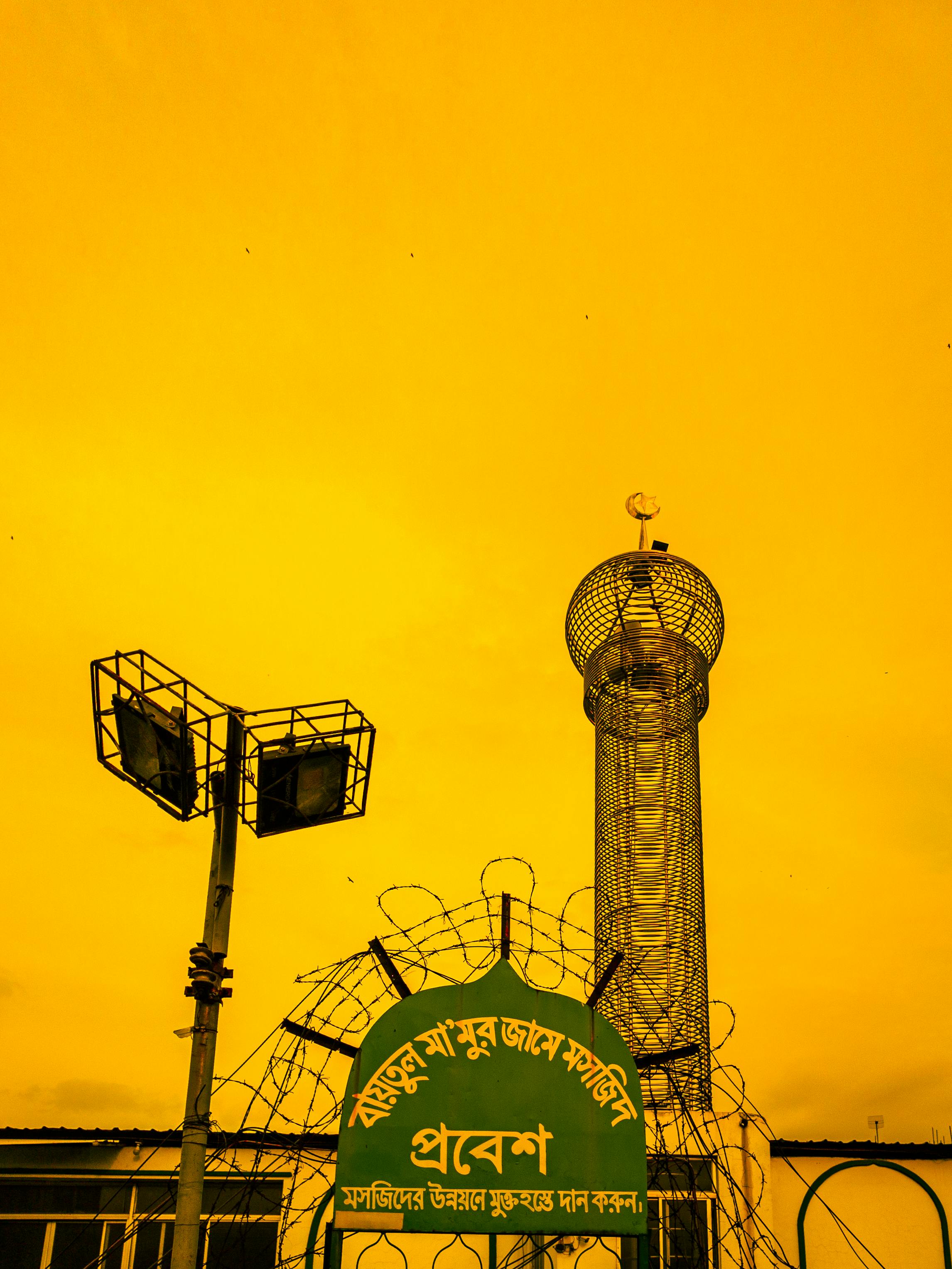 View of a minaret and sign against a vibrant yellow sky in Dhaka, Bangladesh.