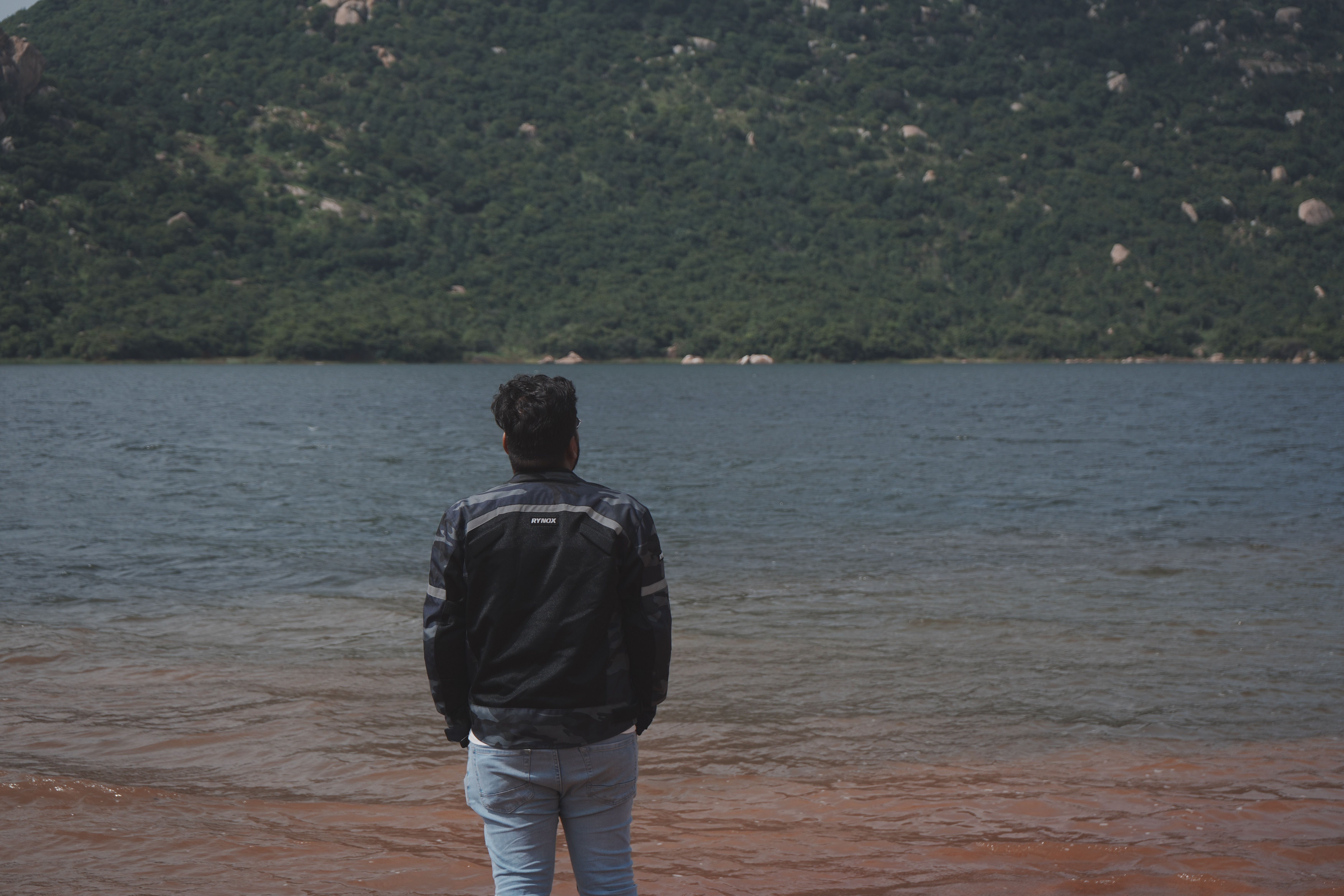 Man Contemplating Scenic Lake and Green Hillside · Free Stock Photo