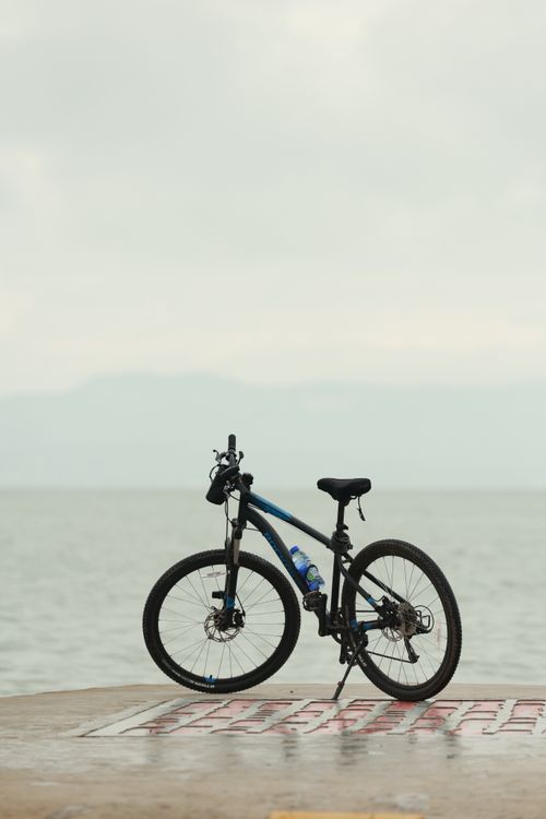 Free Single mountain bike parked on a wet promenade by the sea, under a cloudy sky. Stock Photo