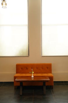 A cozy orange couch with a wooden table and vase in a minimalist indoor setting.