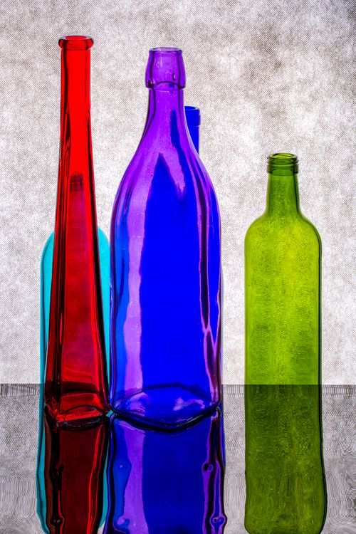 Free Brightly colored glass bottles arranged on a reflective surface, displaying vivid hues. Stock Photo