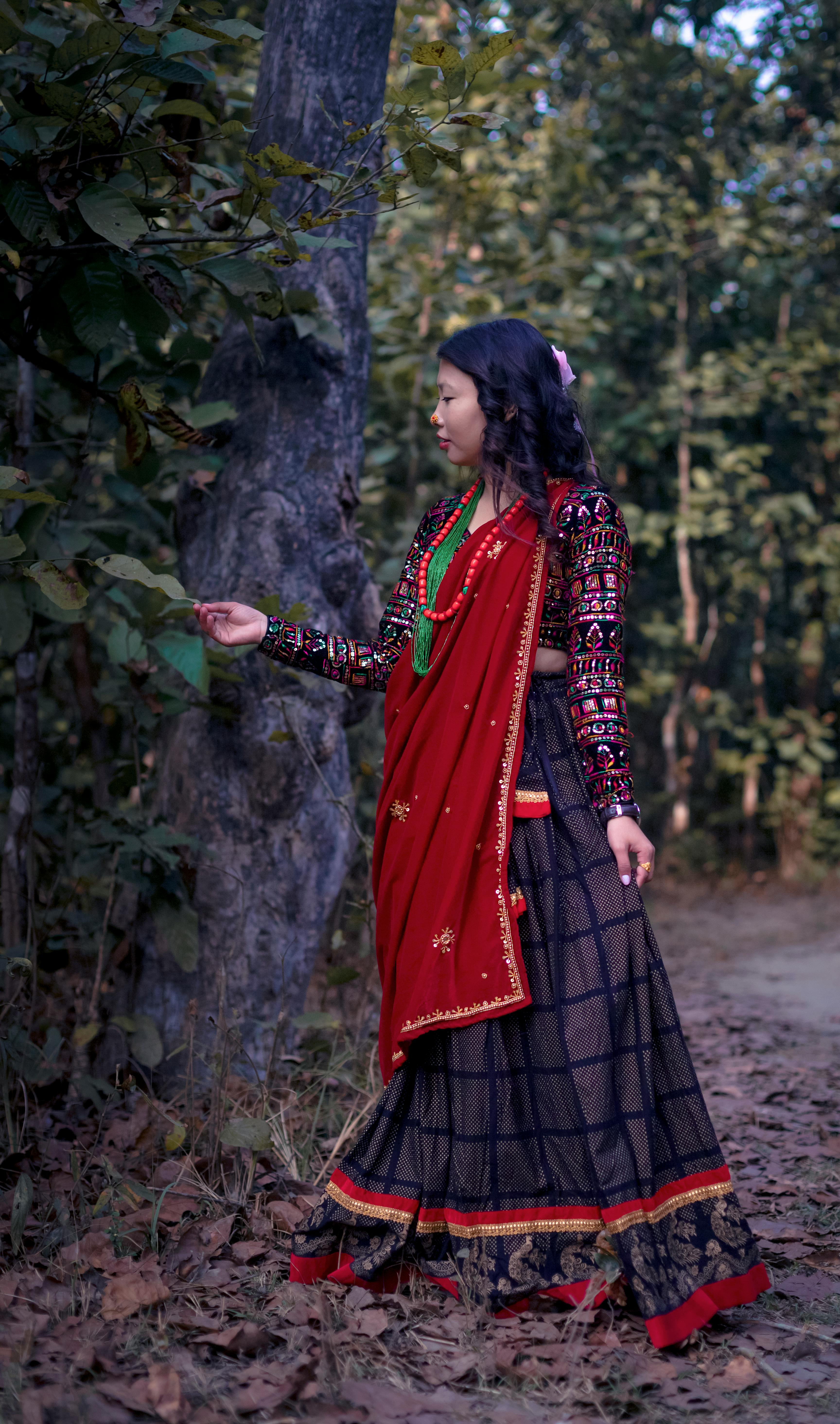 A young woman wearing traditional Nepalese attire poses gracefully in an outdoor forest setting.