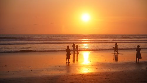 Free Silhouettes of people on a beach during a vibrant sunset. Perfect for travel and leisure content. Stock Photo