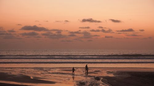 Free A picturesque beach sunset with silhouettes of a family walking along the shore, evoking tranquility and warmth. Stock Photo