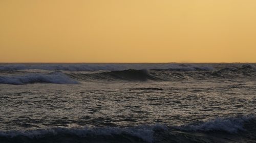 Free Peaceful ocean waves roll under a golden sunset, capturing tranquility. Stock Photo