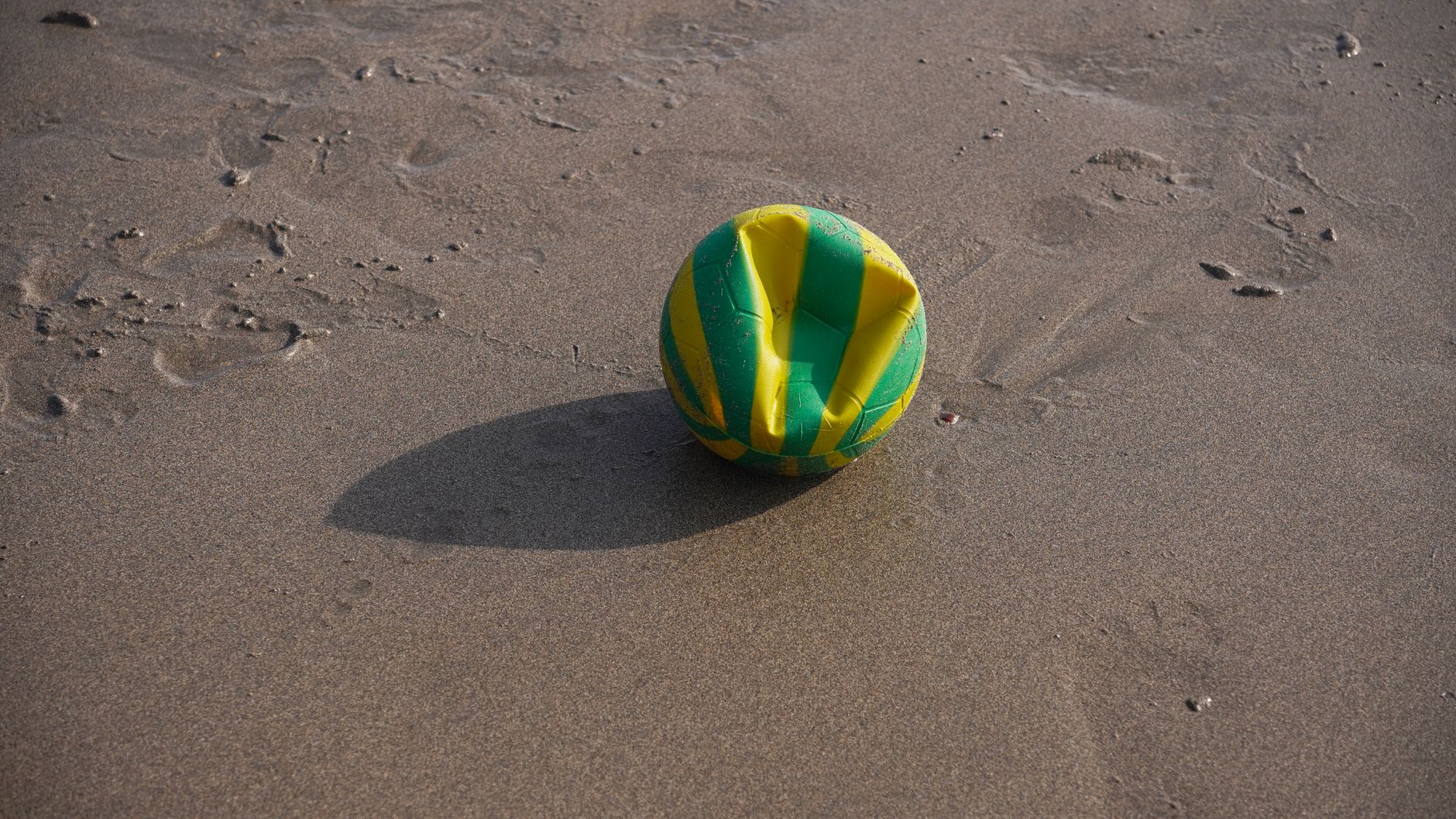 A deflated green and yellow volleyball on a sandy beach, ideal for sports and leisure themes.
