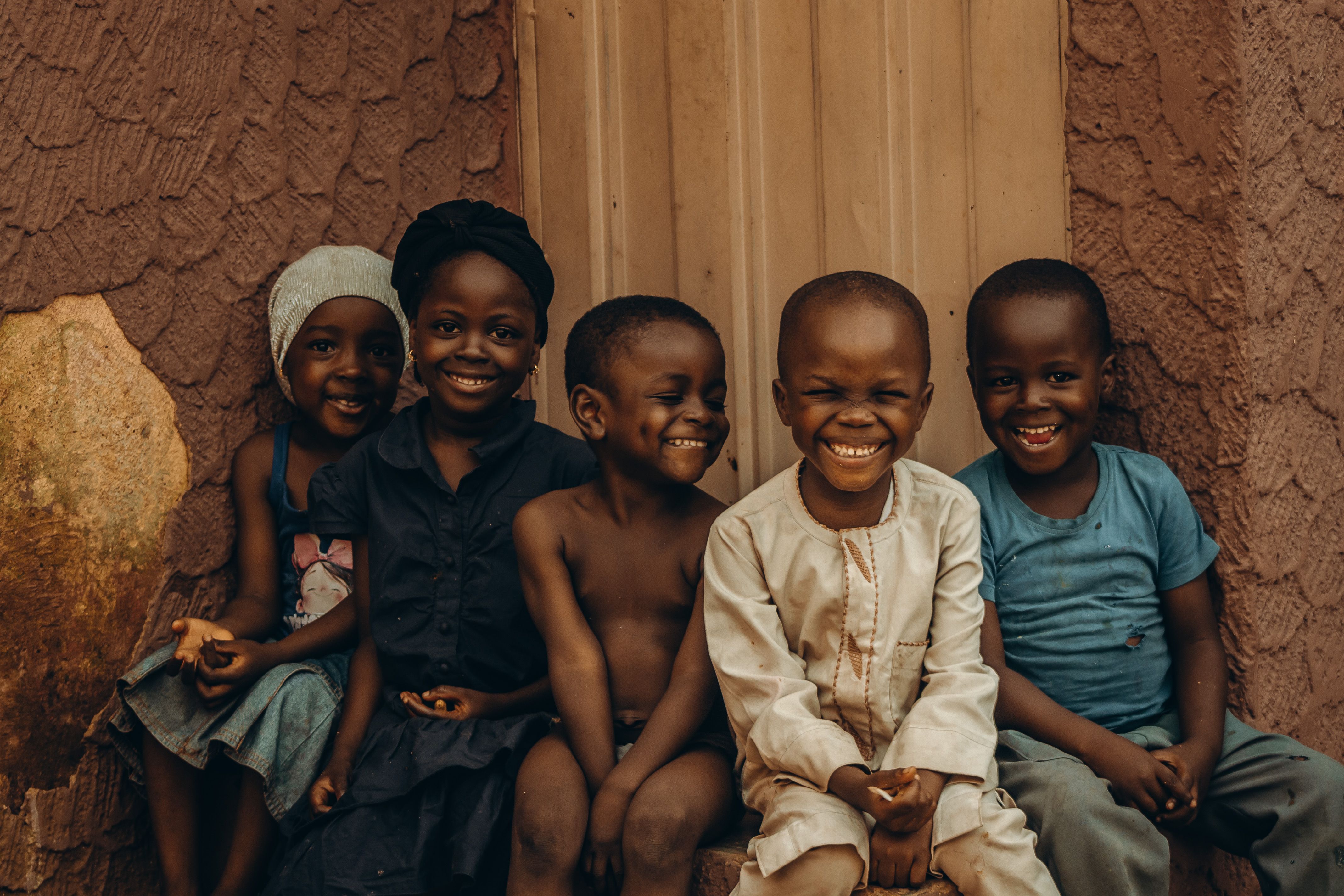 Five children smiling warmly in front of a textured wall, exuding joy and companionship.