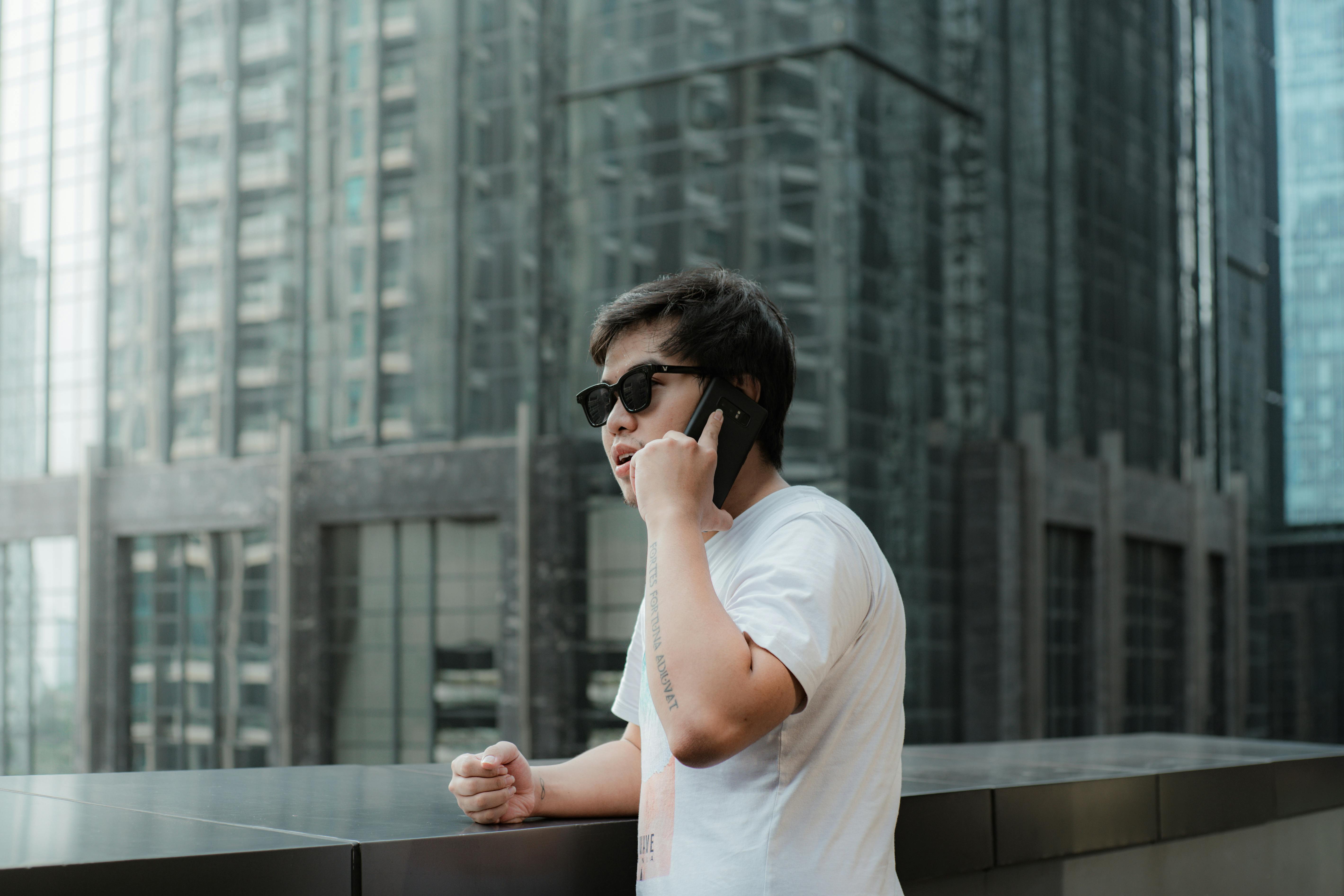 De franc Un jove casual fent una trucada telefònica en un entorn urbà modern amb gratacels. Foto d'estoc