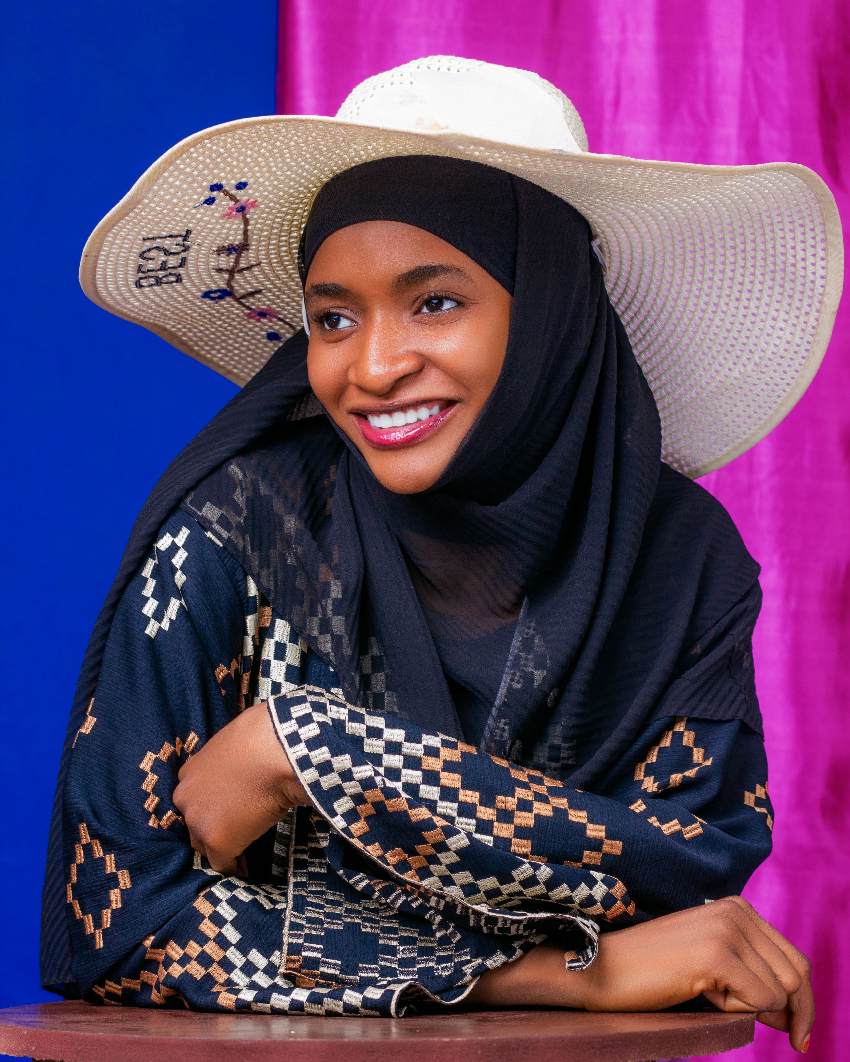 Beautiful woman in cultural dress and hat, beaming with joy indoors.