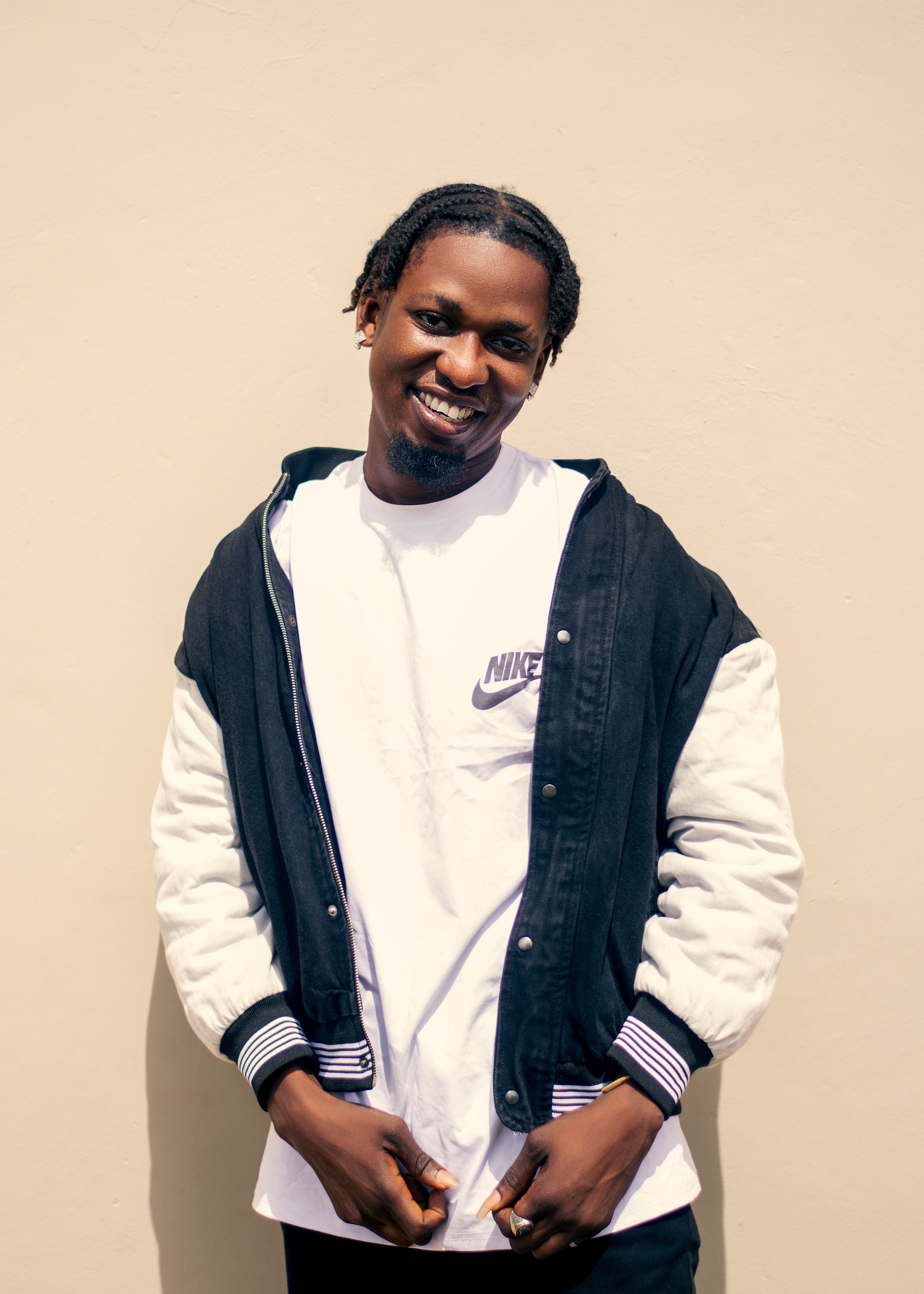 Happy young man with braids smiling in a trendy urban jacket against a plain background.
