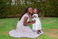 A joyful mother and daughter share a tender moment in a lush garden setting.